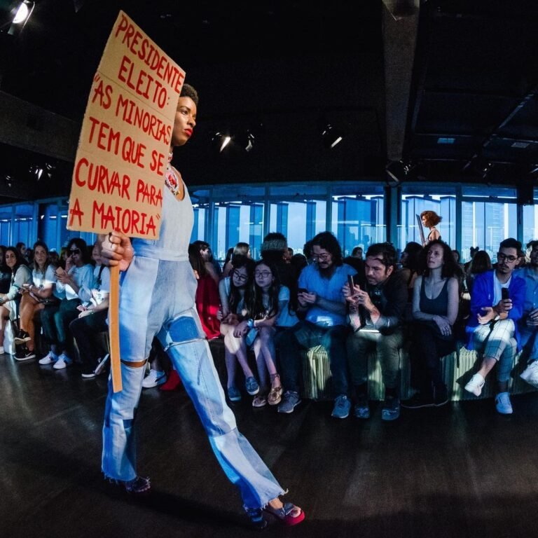 Modelo carrega um cartaz de protesto enquanto desfila de camiseta e jeans.