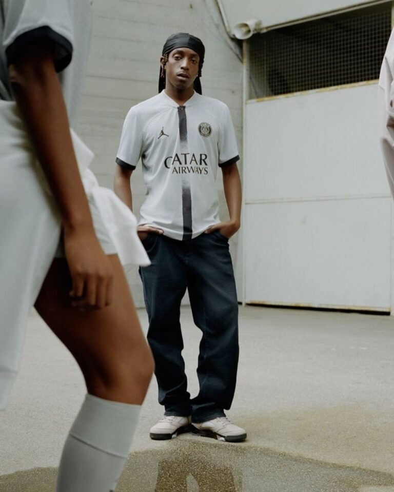 Camisa de futebol branca com faixa escura combinada com calça preta larga.