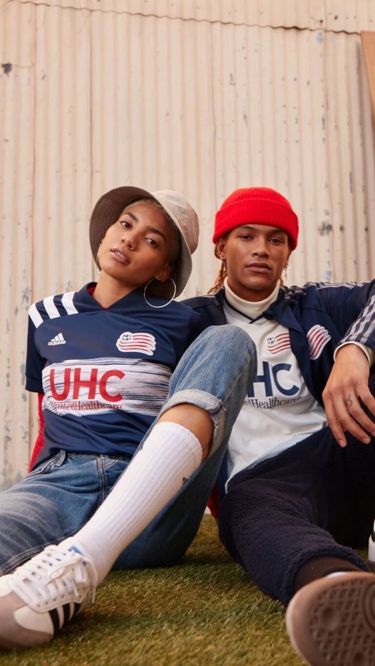 Duas pessoas com camisetas de futebol, boné e boina, sentadas lado a lado.