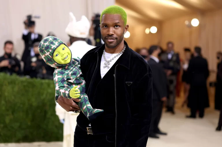 Frank Ocean com terno preto, cabelo verde e uma figura de bebê verde no Met Gala 2021.