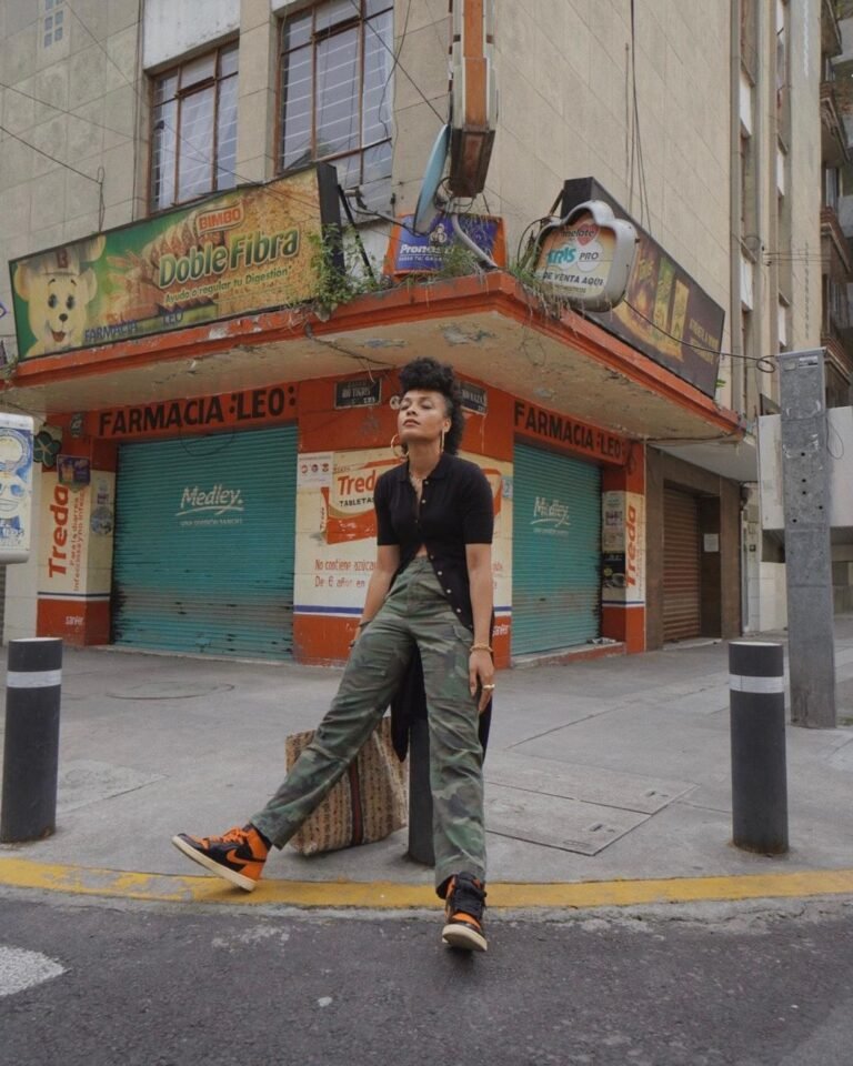Calça larga verde e top preto em uma fotografia na esquina de uma rua.