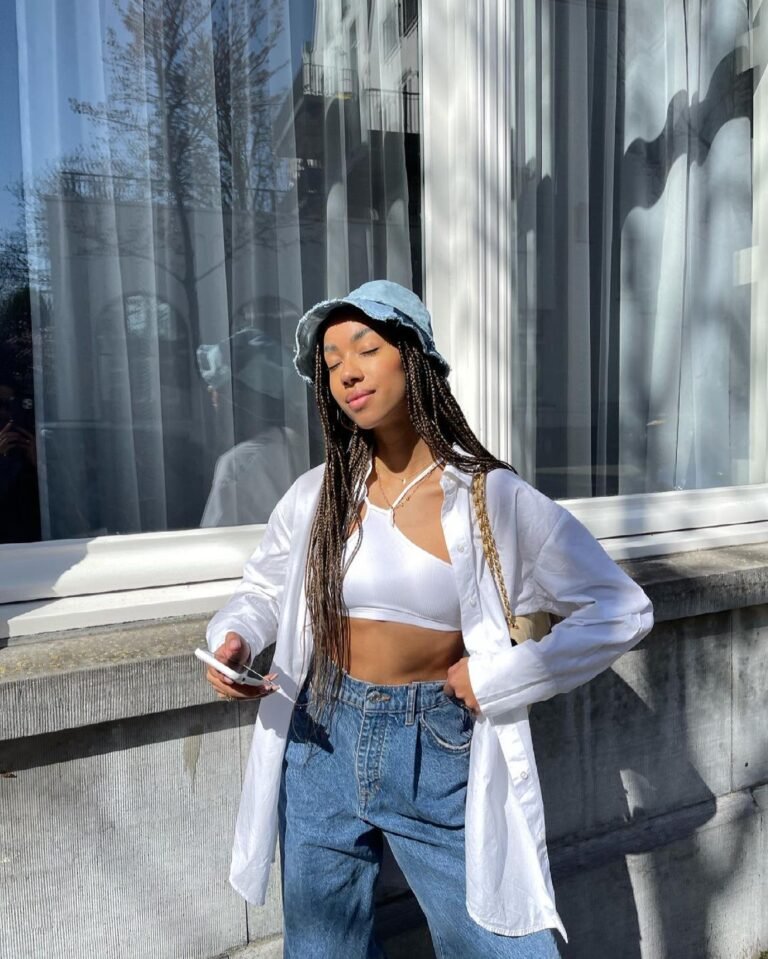 Camisa clara aberta sobre top branco, jeans e chapéu bucket.