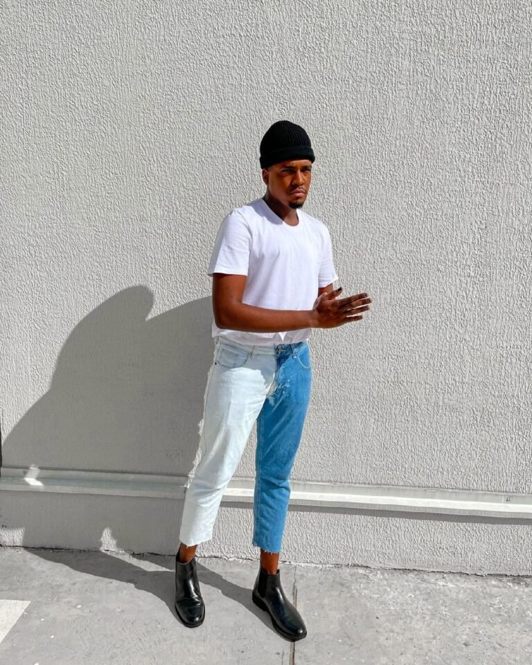 Camiseta branca com calça em dois tons de azul, boné preto e sapatos escuros.
