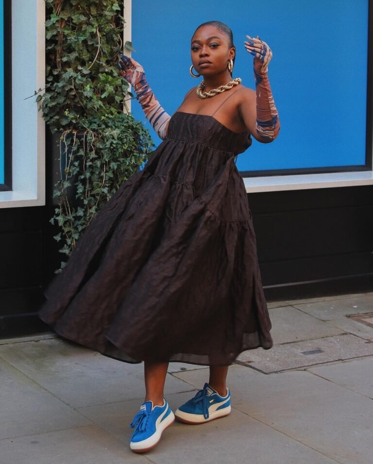 Vestido preto amplo combinado com tênis azuis.