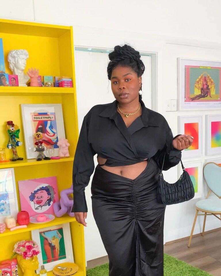 Conjunto preto com blusa amarrada na cintura diante de uma estante amarela.