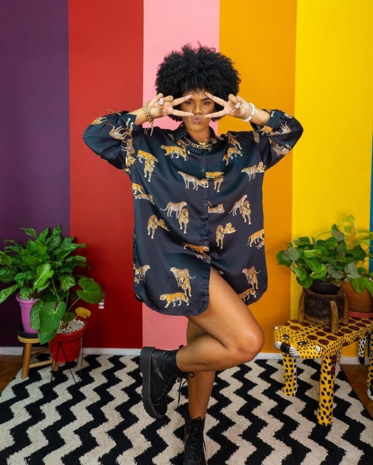 Camisa larga estampada usada como vestido diante de uma parede colorida.