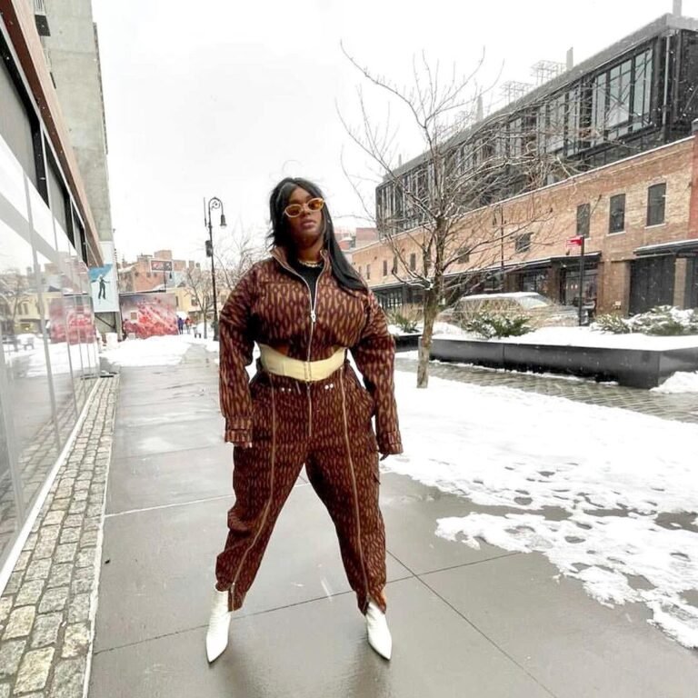 Conjunto marrom estampado com cinto amarelo e botas brancas em uma rua com neve.