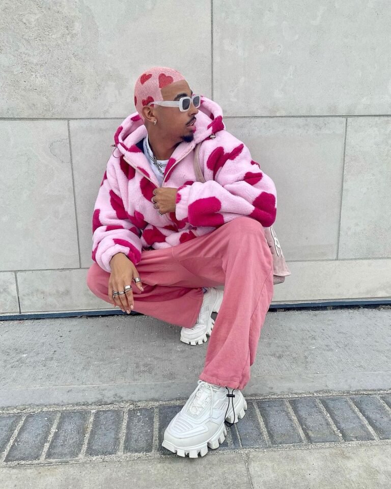 Look rosa com casaco estampado e tênis brancos, em um retrato sentado.