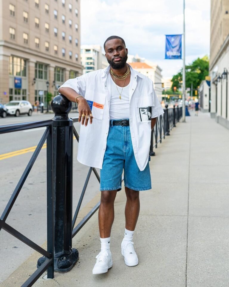 Camisa branca aberta sobre camiseta, bermuda azul e meias altas com tênis brancos.