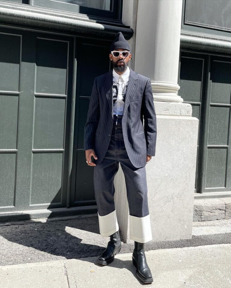 Terno escuro com calça de barra clara, chapéu e botas em uma fotografia na rua.