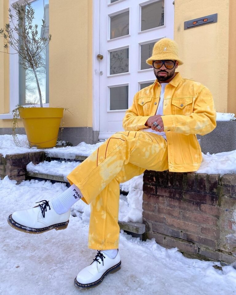 Conjunto amarelo com jaqueta, calça e chapéu bucket em um cenário com neve.