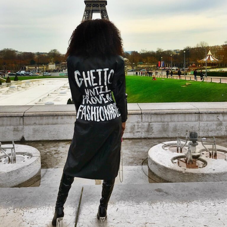 Pessoa de costas com casaco preto estampado com a frase “Ghetto Until Proven Fashionable”.