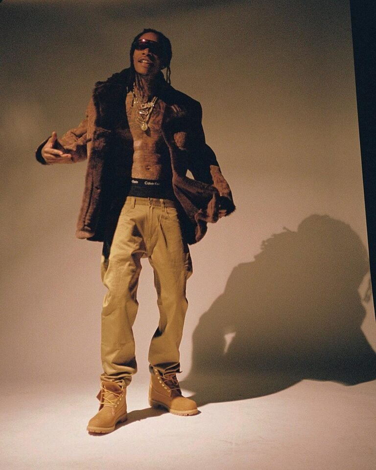 Look com jaqueta aberta, calça bege e botas Timberland em um estúdio.