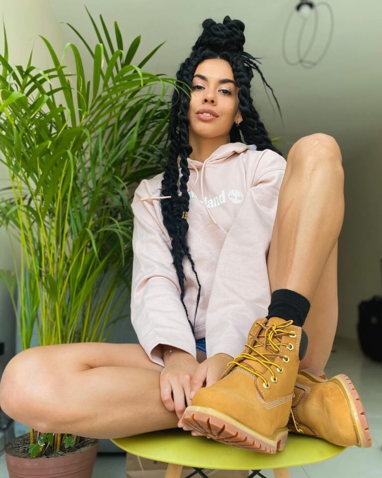 Botas Timberland amarelas usadas com camisa clara em um retrato sentado.