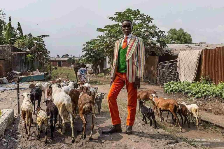 Look La Sape com blazer claro, calça laranja e gravata, ao lado de animais em uma rua.