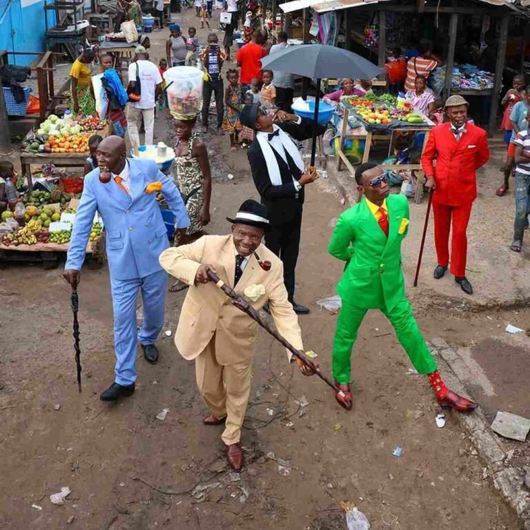 Grupo de sapeurs com ternos coloridos caminhando por uma rua com feira.