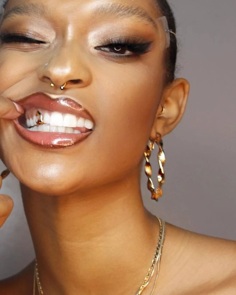 Sorriso com grillz nos dentes superiores, argolas e piercing no nariz.