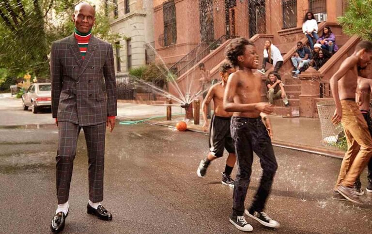 Dapper Dan de terno em uma rua do Harlem, com moradores ao fundo.