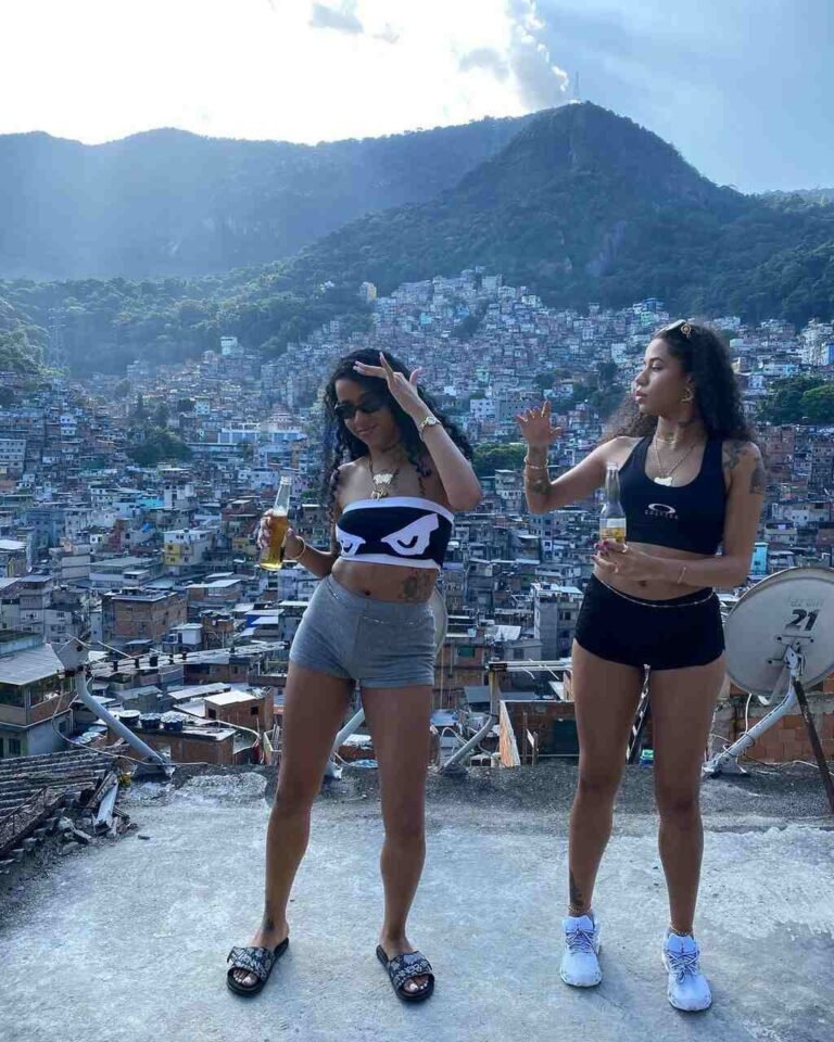 Tasha e Tracie mostram looks com tops, shorts e tênis diante de uma paisagem urbana.