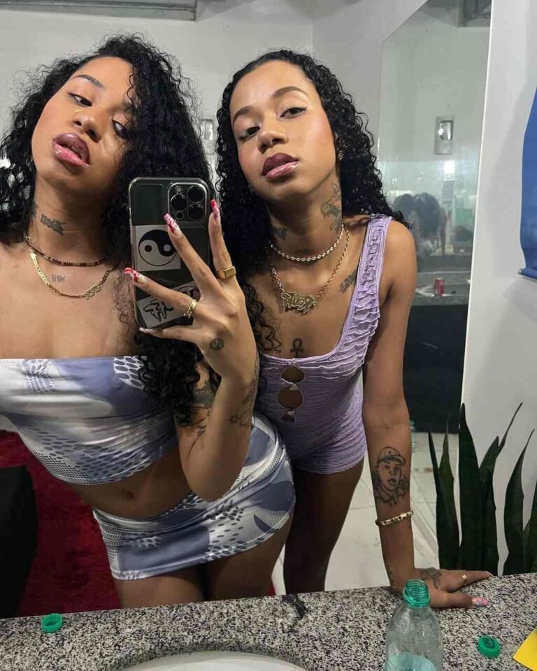Tasha e Tracie com tops curtos e calças jeans em uma selfie no espelho.