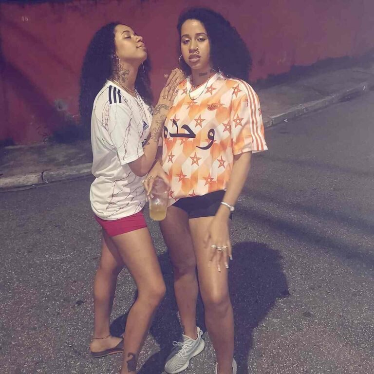 Tasha e Tracie com camisetas estampadas e shorts em uma fotografia noturna.