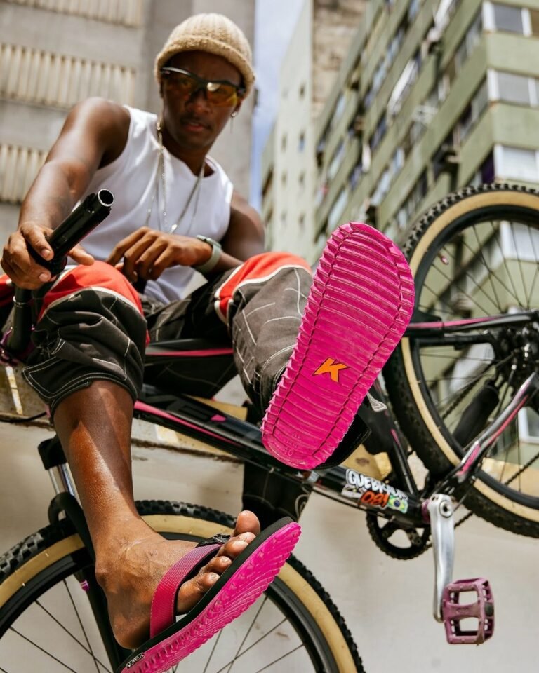 Sandália Kenner de sola rosa em primeiro plano, junto a uma bicicleta na rua.