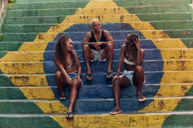 Três pessoas de sandálias Kenner sentadas em uma escadaria pintada com a bandeira do Brasil.