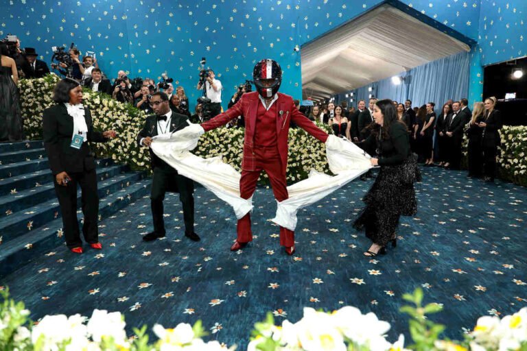 Damson Idris de terno vermelho com uma longa cauda branca no Met Gala 2025.