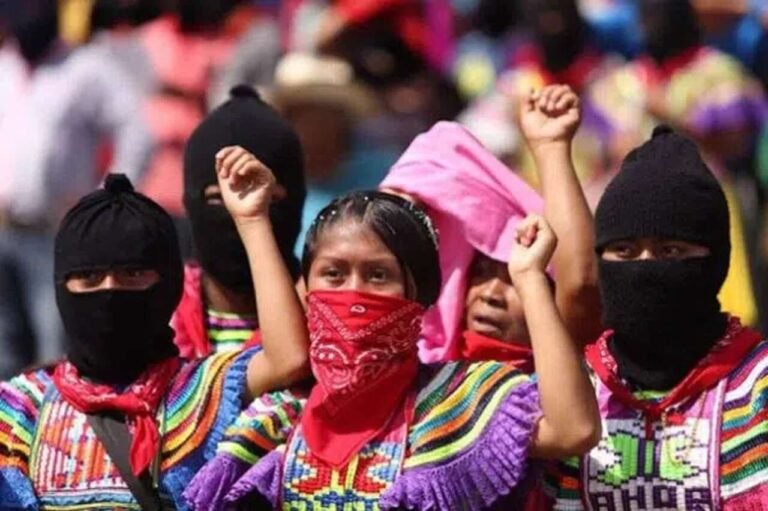 Manifestantes com bandanas vermelhas e pretas cobrindo o rosto e punhos erguidos.