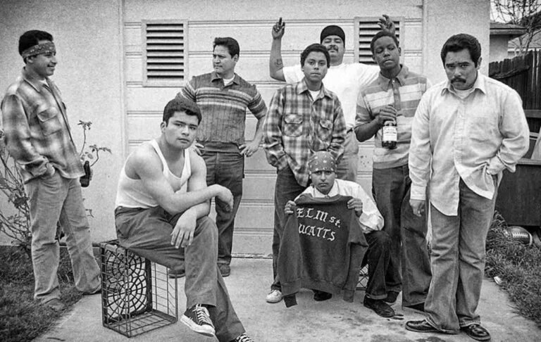 Fotografia em preto e branco de um grupo com camisas xadrez, bonés e bandanas.
