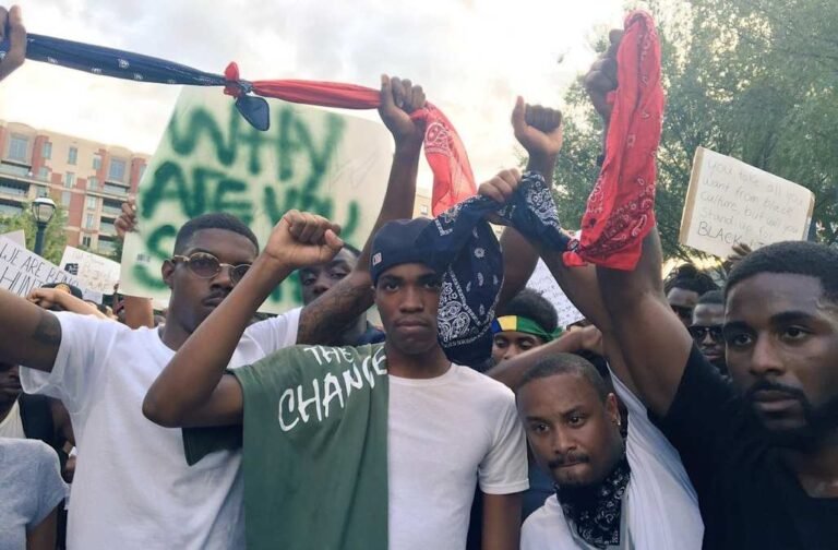 Grupo com bandanas azuis e vermelhas reunido em uma manifestação.