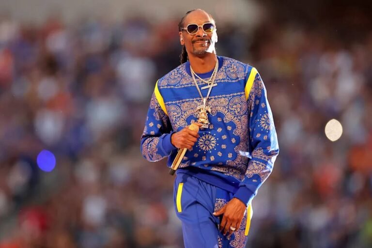 Snoop Dogg de conjunto azul com estampa de bandanas durante uma apresentação.